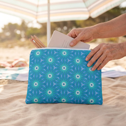 Large Sapphire Nebula accessory pouch (11.81 × 8.35 inches) in use: woman puts a paperback-size notebook and pencils into pouch, no loose sand touching it. Lifestyle mockup with hands showing scale.