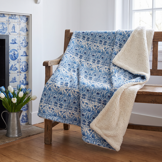 Dutch Blue Tulip sherpa fleece blanket on a farmhouse bench beside a delft-tiled hearth with fresh tulips