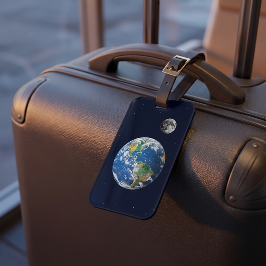 Cosmic Traveler acrylic luggage tag at true size on a hard-shell carry-on at dusk