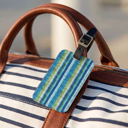 Ocean Whisper Stripes acrylic luggage tag at true size on a striped canvas duffel by the water