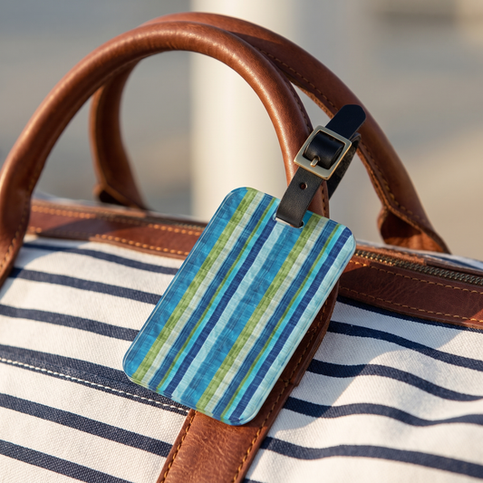 Ocean Whisper Stripes acrylic luggage tag at true size on a striped canvas duffel by the water