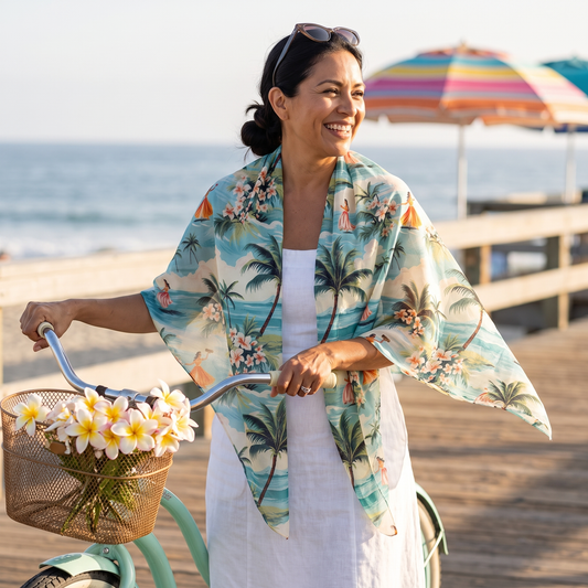A woman with a vintage cruiser bicycle on a seaside boardwalk, wearing the Retro Hawaiian Hula 50-inch square voile scarf open over her shoulders, corners lifting in the breeze