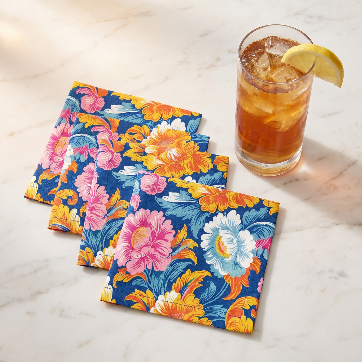 Chintz Charm cocktail napkins, set of four, fanned beside a glass of iced tea on pale marble